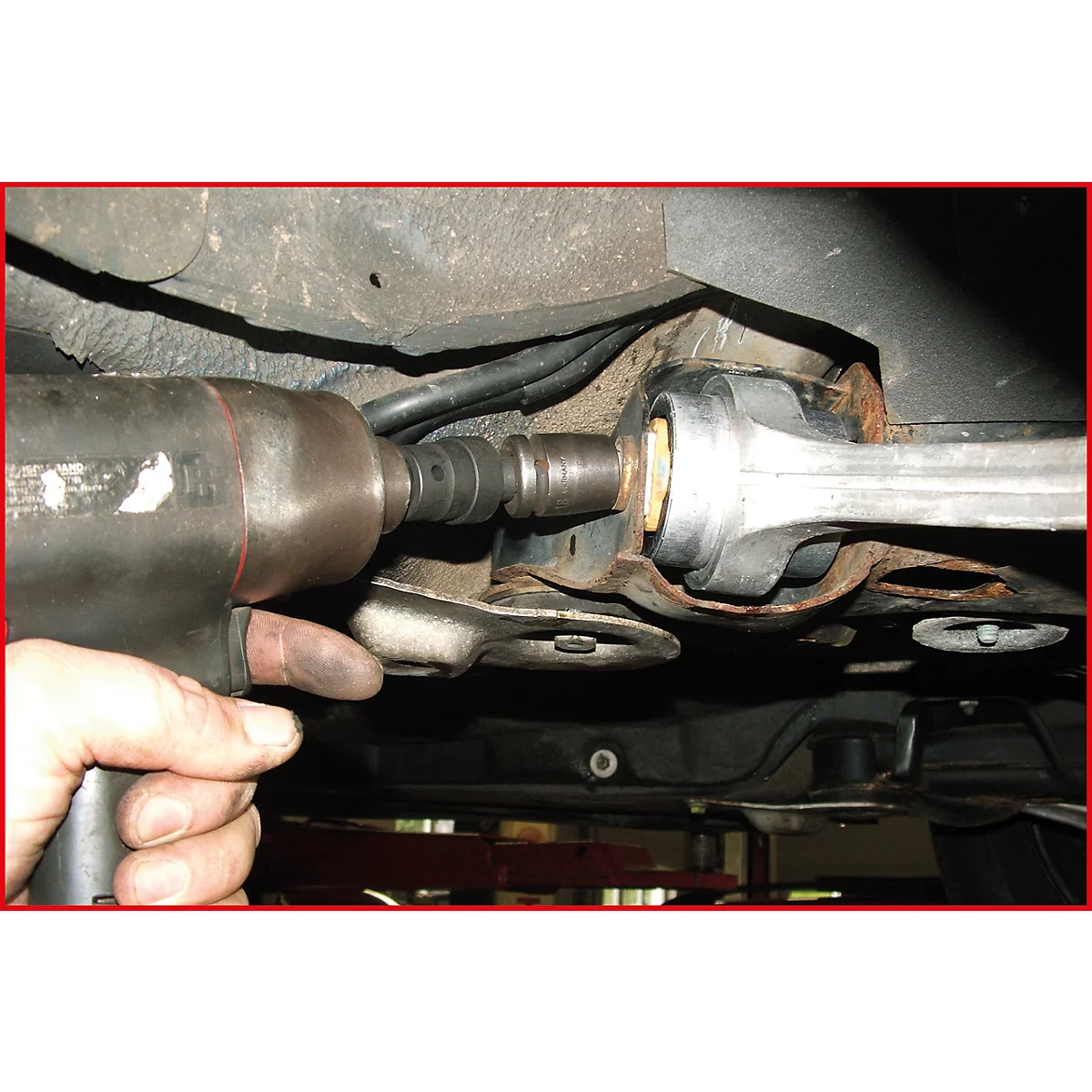 Ein Mechaniker verwendet einen Schlagschrauber, um ein Fahrwerksteil an einem Fahrzeug zu lösen.